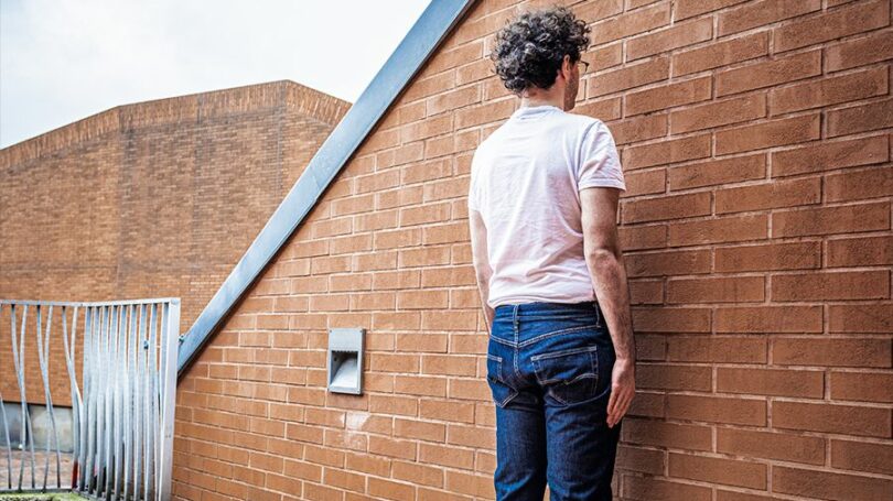 Ein Mann in Jeans steht mit Gesicht zu einer Ziegelwand